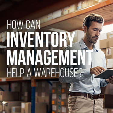 A man keeping track of inventory while walking through a warehouse of boxes stacked on shelves