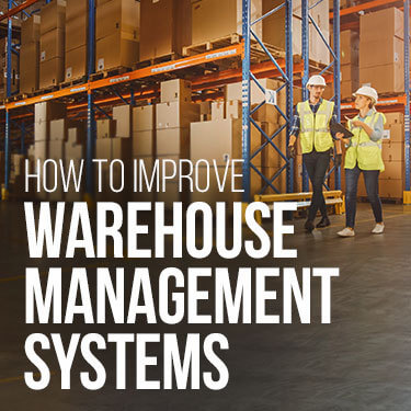 Two warehouse workers in safety gear walking through a warehouse with boxes stacked on shelves