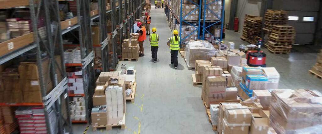 Six warehouse workers in an aisle at a warehouse. 