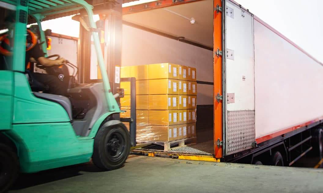 A forklift loading a pallet into a dry van trailer