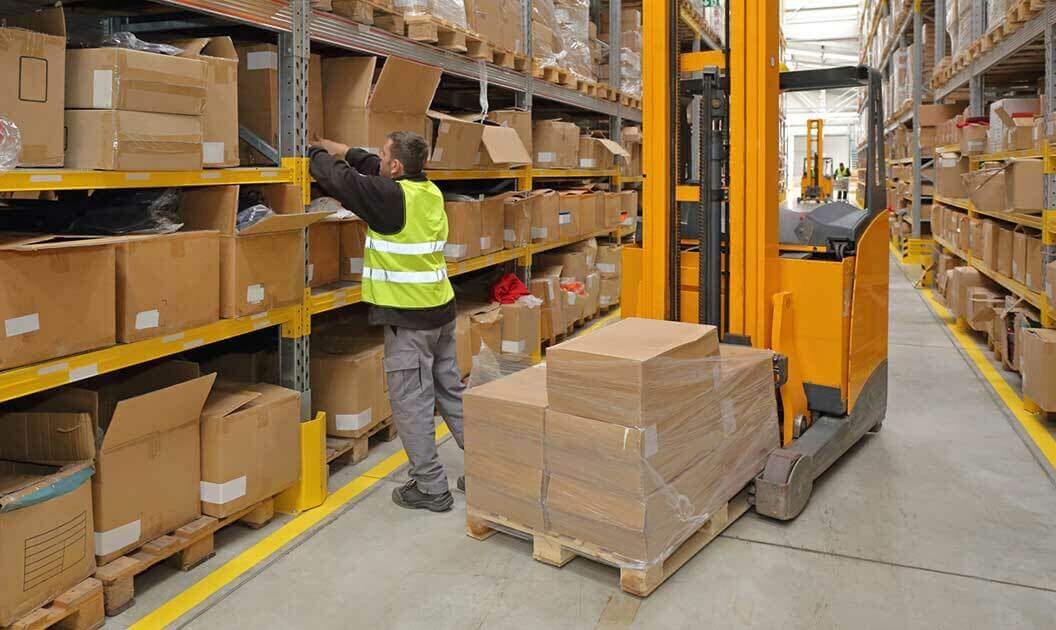 A warehouse employee standing next to a forklift.