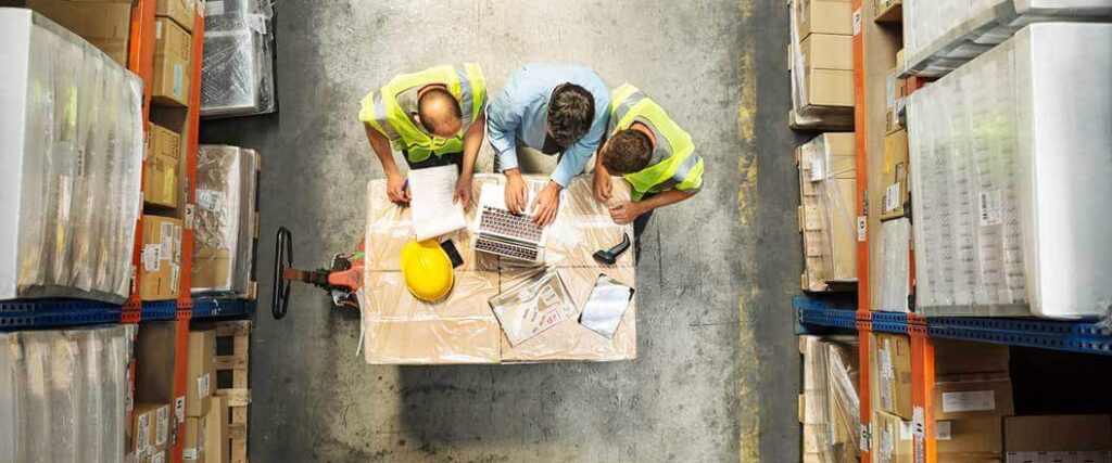 Three warehouse workers checking information on a laptop. 