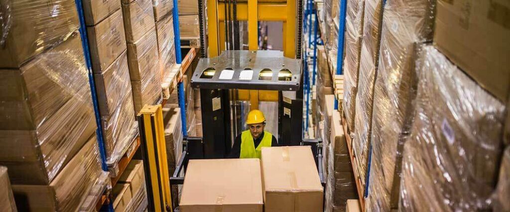 A forklift operator in a retail shipping warehouse loading palletized freight onto a shelf